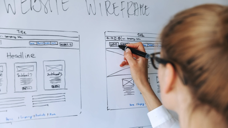 A young woman sketches the wireframe of a website on a whiteboard.