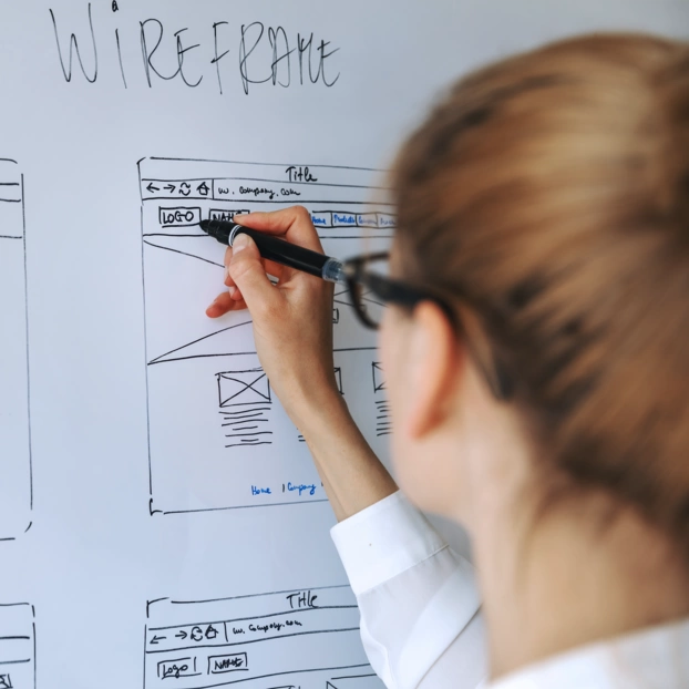 A young woman sketches the wireframe of a website on a whiteboard.