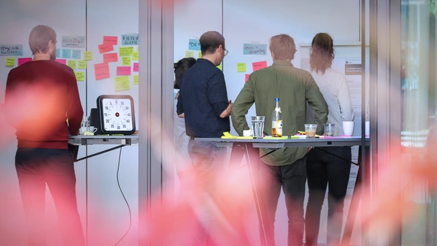 In a digitization lab, people collect ideas on a large wall. View from outside into the large event room.