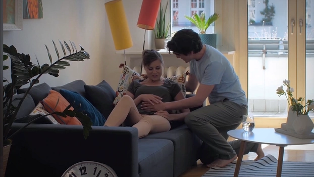 A pregnant woman with her boyfriend or husband in the apartment. He lovingly caresses her belly. 