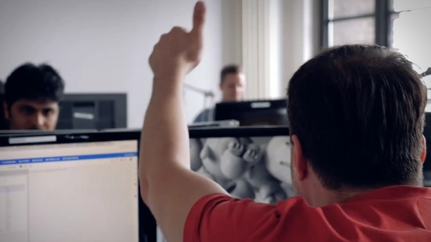 A muslim employee smilingly looks at a person not visible in the picture. She is sitting at a desk with two screens.