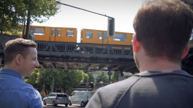 Zwei Kollegen gehen am Schlesischen Tor in Berlin in die Mittagspause. Im Hintergrund ist die U-Bahn auf der Hochbahn zu sehen.