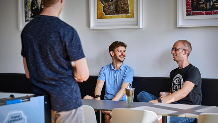 Three employees are chatting in the office kitchen.