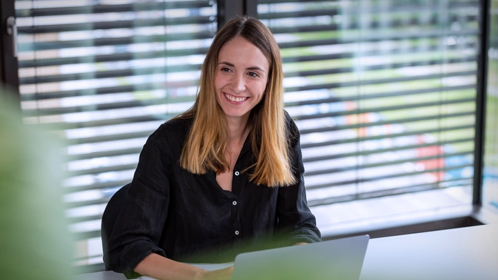 UX designer Nicole Lössner works in the office. She smiles at a person who is not visible in the picture.