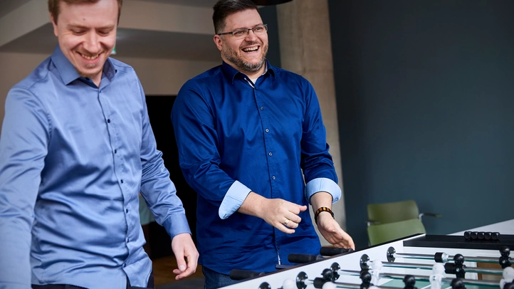 Zwei Kollegen am Standort Hamburg spielen Kicker in der großen Küchenzone.