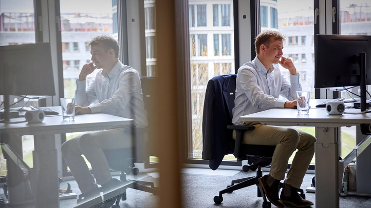 A colleague at the Hamburg site works at a PC in an office with a large glass front.