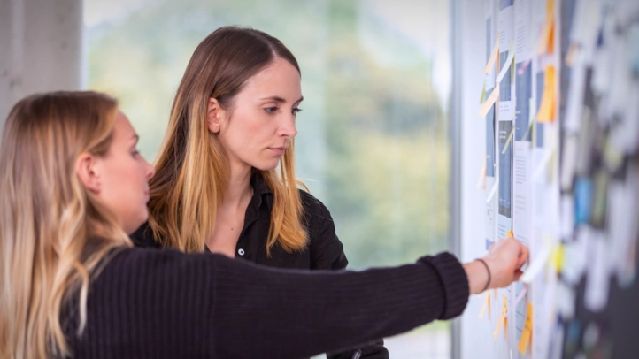 A UX consultant and a designer evaluate project approaches using a mood board on the wall.