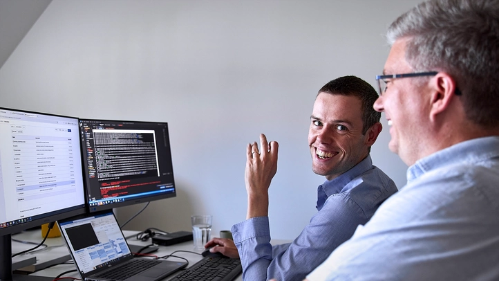Zwei Leipziger Kollegen diskutieren am Arbeitsplatz. Auf dem Bildschirm ist Programmcode zu sehen.