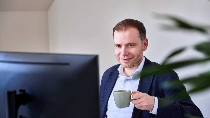 Mann mit Kaffeetasse vor Bildschirm