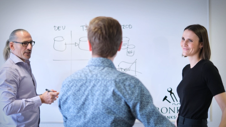 Three employees of Ironforge are discussing in front of a whiteboard.