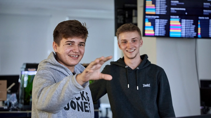 Two employees from the team Operations are talking to a person who is not visible in the picture. In the background, a monitoring dashboard is blurred on a screen.