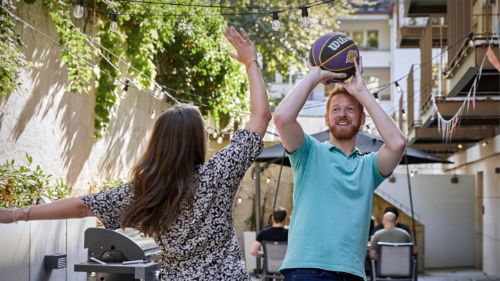 Eine Mitarbeiterin und ein Mitarbeiter am Kölner Standort von ]init[ spielen Basketball im Innenhof.