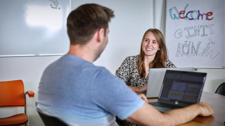 An employee at the Cologne office is discussing with a colleague in the meeting room.