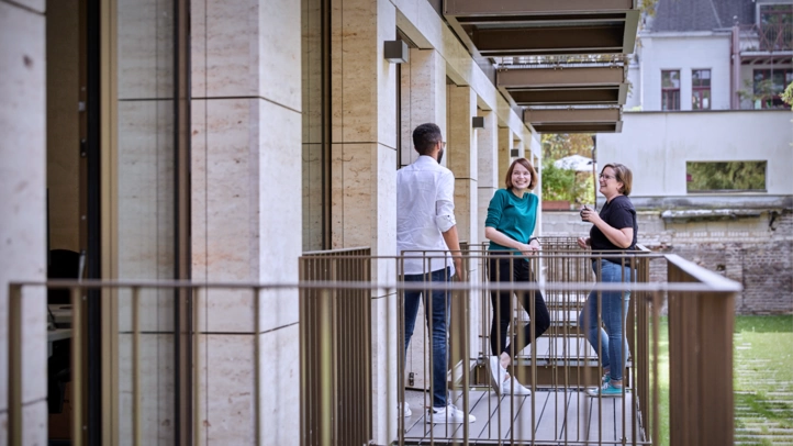 Employees at the Cologne site take a break on a balcony with a view of the green courtyard.
