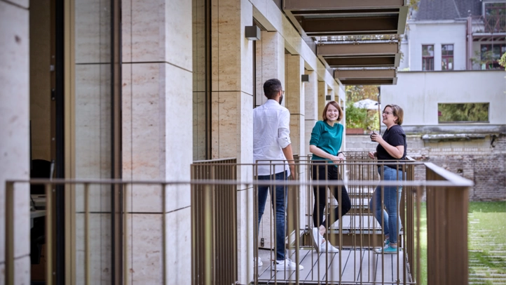 Mitarbeiter:innen am Kölner Standort machen Pause auf einem Balkon mit Blick in den grünen Innenhof.