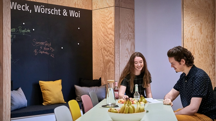 Eine Mitarbeiterin und ein Mitarbeiter unterhalten sich sitzend in einer der modern eingerichteten Küchen- und Aufenthaltsbereiche am Mainzer Standort.
