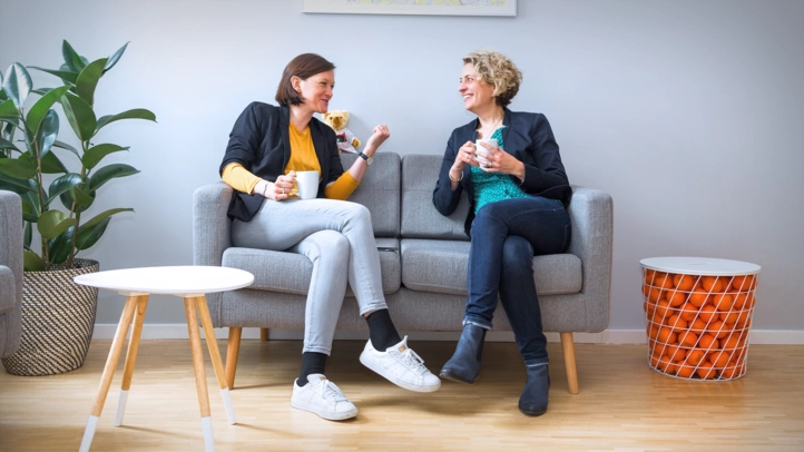 Zwei Mitarbeiterinnen am München Standort unterhalten sich auf einer Couch.