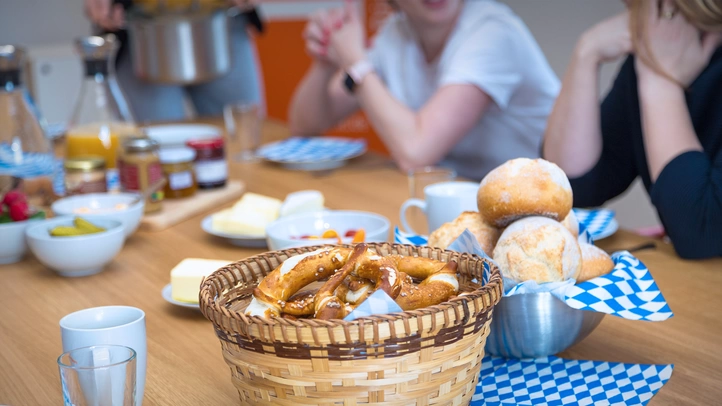 Brotzeit am Münchner Standort. Zu sehen sind Brezeln, Brötchen und Deftiges auf Tischdecken mit den bayrischen Landesfarben in Blau und Weiß.