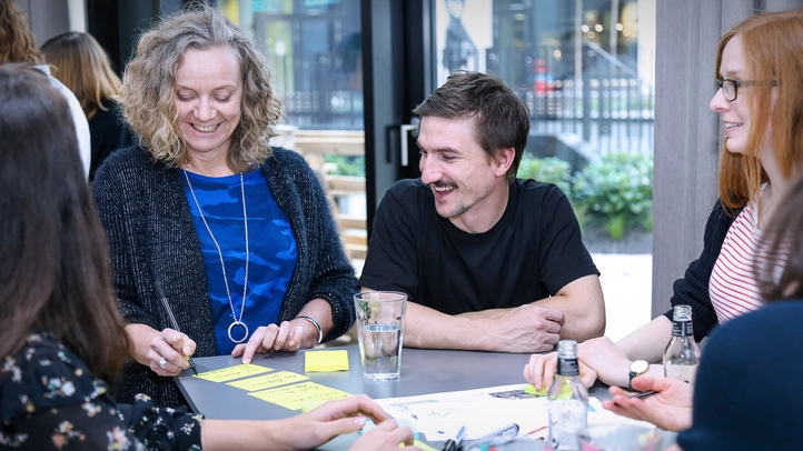 Drei Mitarbeiterinnen und ein Mitarbeiter diskutieren auf einem Workshop miteinander.