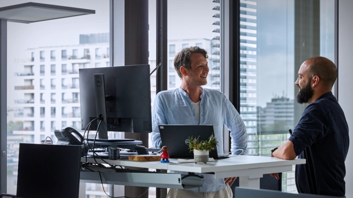 Zwei Mitarbeiter unterhalten sich im Büro am Schreibtisch.