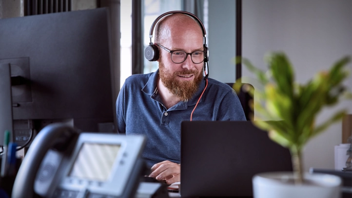 Ein Mitarbeiter arbeitet im Büro. Er schaut auf seinen Laptop und trägt ein Headset.