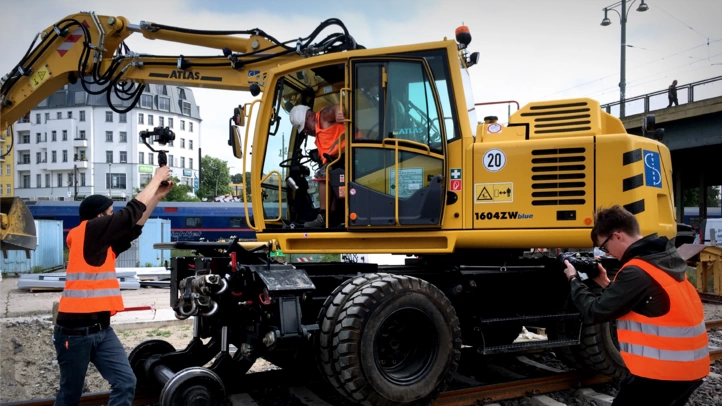 Two video producers from ]init[ shoot in front of a two-way excavator on the Berlin city railroad.