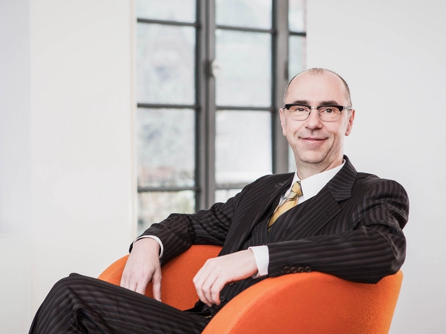 Dirk Stocksmeier, the chairman of the supervisory board of ]int[ AG is sitting in his office in an orange armchair.