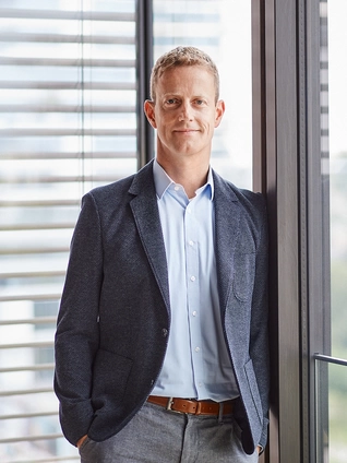 Gregor Költzsch, Chief Business Officer of ]init[ AG, stands in front of a fully glazed facade in his office in Berlin.