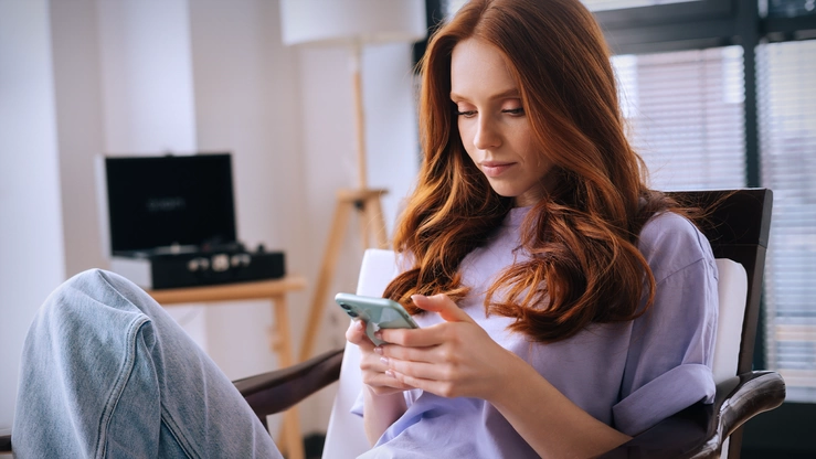 Eine junge Frau surft zuhause auf ihrem Smartphone.