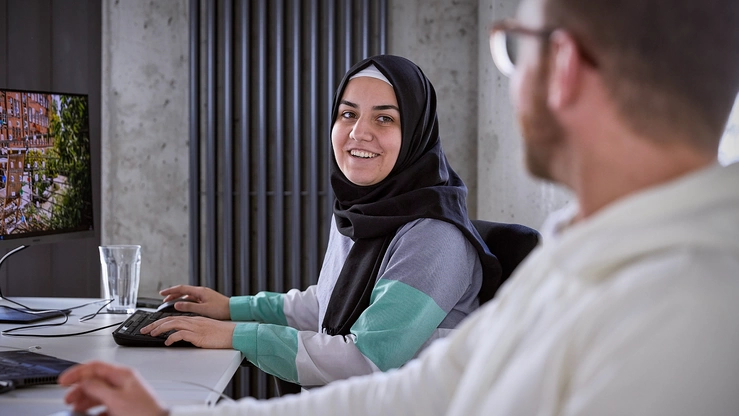 Eine muslimische Mitarbeiterin mit Kopftuch bespricht sich mit einem Kollegen am Arbeitsplatz.