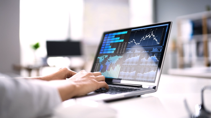 A laptop with a data dashboard with various graphs and performance indicators from the stock market environment. A person's hand is typing on the keyboard.