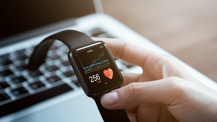 Eine Hand hält eine Smartwatch mit einer Gesundheitsapp. Auf dem Bildschirm ist ein Dashboard mit Fitnessdaten zu sehen.