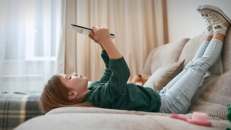 Ein Schulkind spielt liegend auf einem Tablet.