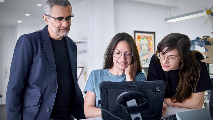 Drei Personen im Büro auf ein Tablet schauend