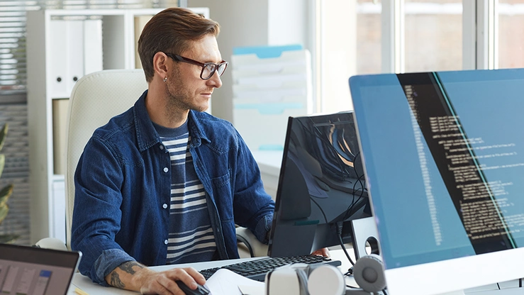 Mann sitzt am Arbeitsplatz mit Bildschirm