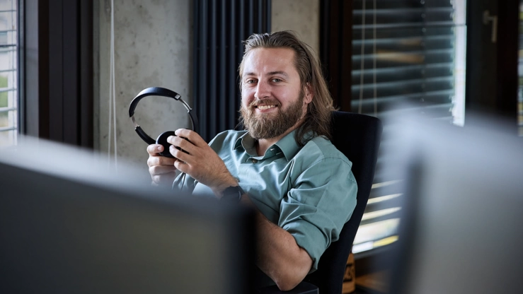 Ein Berater sitzt im Office und unterhält sich mit einer Person, die nicht im Bild sichtbar ist. Er hält ein Headset in der Hand.