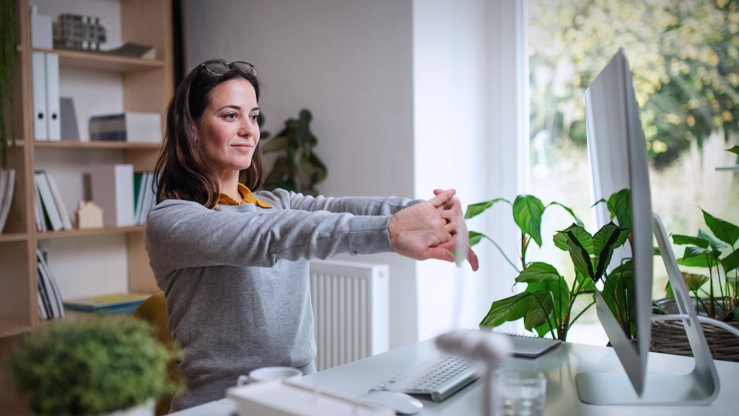 Eine Frau arbeitet im Home Office. Sie macht vor ihrem Arbeitsplatz Entspannungsübungen.