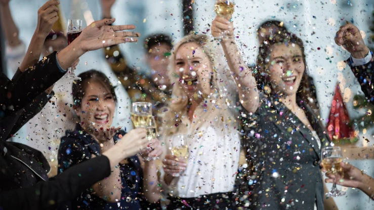 Employees celebrate a success in the office! Confetti flies around the room, colleagues toast with champagne.