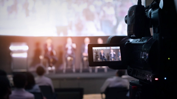 Eine Kamera mit Vorschaudisplay filmt eine Podiumsdiskussion.