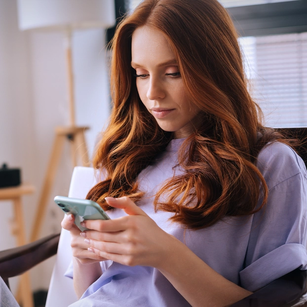 Eine junge Frau surft zuhause auf ihrem Smartphone.