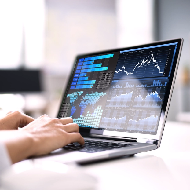 A laptop with a data dashboard with various graphs and performance indicators from the stock market environment. A person's hand is typing on the keyboard.