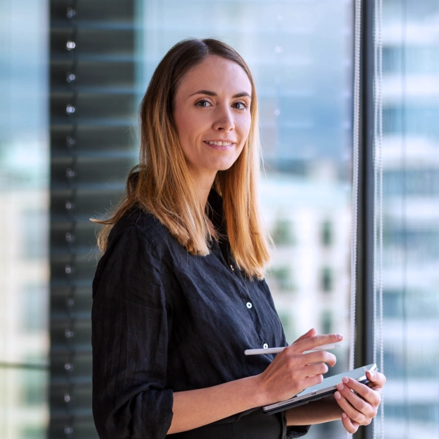 Die UX Designerin Nicole Lössner steht mit einem Tablet im Office. Im Hintergrund ist die Innenstadt Berlins zu sehen.