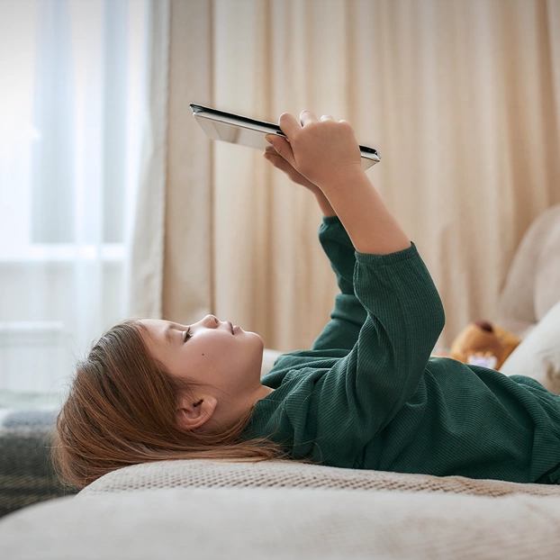 Ein Schulkind spielt liegend auf einem Tablet.