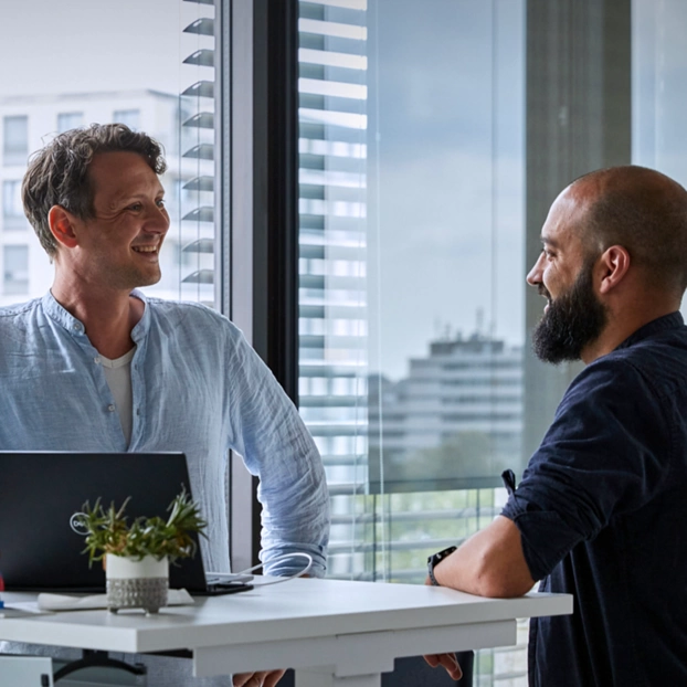 Zwei Personen unterhalten sich am PC-Arbeitsplatz.