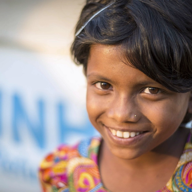 Ein Mädchen aus Myanmar sitzt vor einem Plakat der UNO-Flüchtlingshilfe.