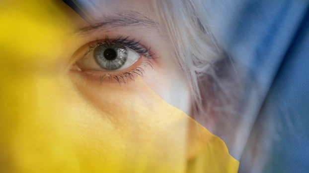 Die gelb-blaue ukrainische Flagge, überblendet mit dem Gesicht einer Frau.