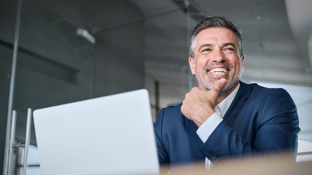 Ein Geschäftsmann sitzt freudig lachend vor einem geöffneten Laptop.