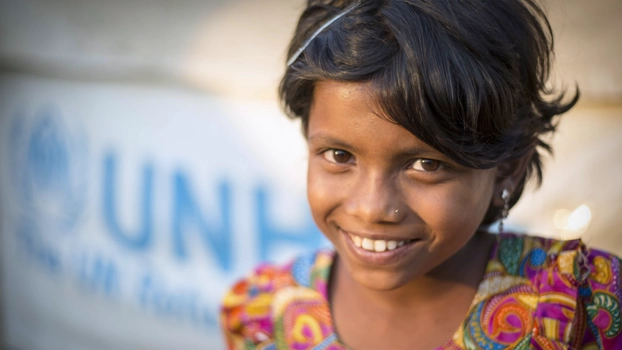 Ein Mädchen aus Myanmar sitzt vor einem Plakat der UNO-Flüchtlingshilfe.
